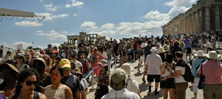 A wide-angle shot of an extremely crowded scene of people visiting the Acropolis at the entrance in Athens, with visitors clustered around the base of ancient columns and structures.