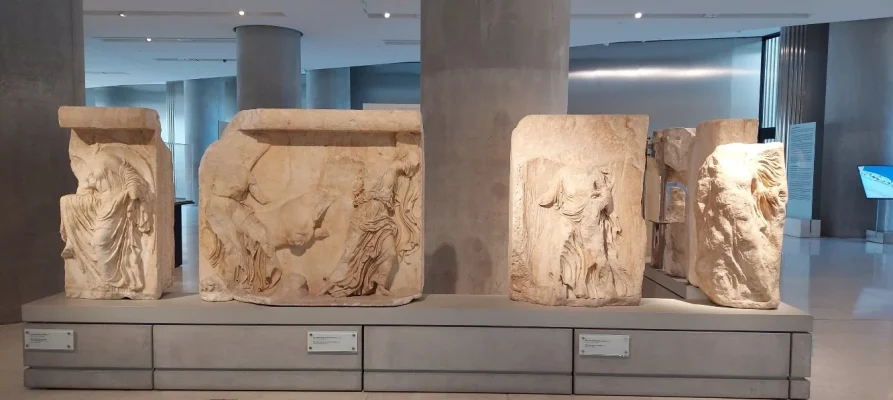 Nike adjusting her sandal, two Nike leading a bull to sacrifice, nike mounting a stairway at the Acropolis Museum in Athens