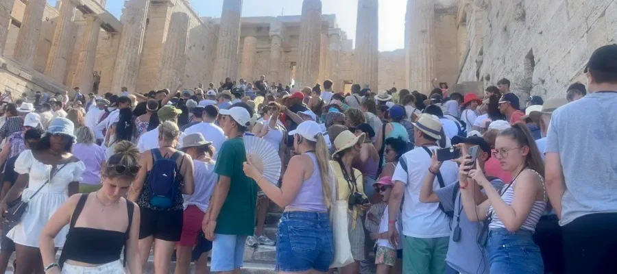 Photo capturing a dense crowd of tourists ascending the steps of the Acropolis in Athens, with the ancient columns lining the path under a bright sun.