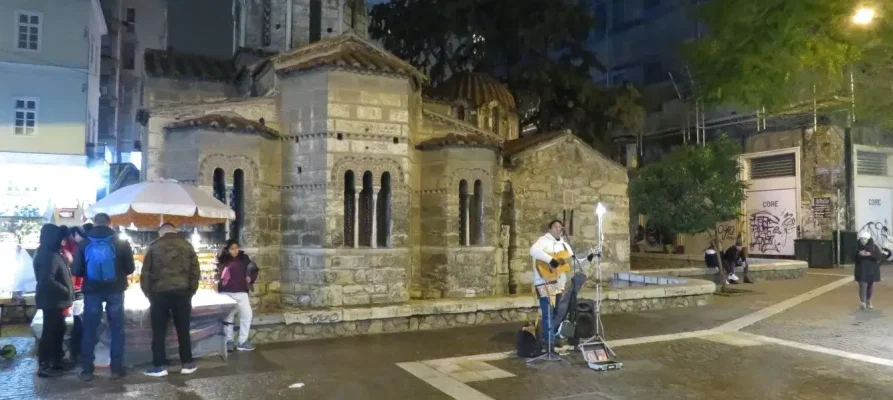 At night, the Church of Panagia Kapnikarea in Athens with a street entertainer playing