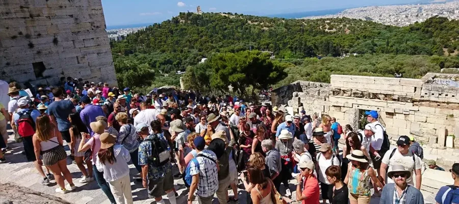 visitors in summer attire walking through a narrow walkway towards the Acropolis of Athens